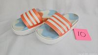 Pair of Adidas slides with orange and white striped straps, blue and orange footbed pattern, white sole