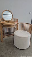 Vanity with round foldable mirror and white upholstered stool next to it.