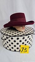 Front view of burgundy felt hat placed on polka dot hat box showing the hat shape and ribbon band.
