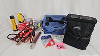 Fully laid out emergency car kit contents including flashlights, jumper cables, first aid kit, safety vest, poncho, flares, and carry bags.