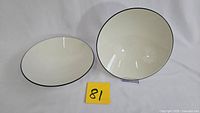Two ivory ceramic bowls with black rims photographed on white backdrop, marked with lot number 81.