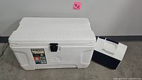 White Igloo Marine Ultra cooler with textured lid and navy latch, along with smaller white and navy Igloo Playmate cooler next to it.
