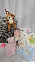 Overall contents of the baby gift basket with plush toys and blankets, including the large woven basket with the brown dog plush hanging on it, and blankets and plush toys arranged inside and around the basket.