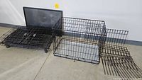 Medium and large collapsible metal wire dog crates with plastic floor pans, one crate equipped with wheels, displayed unfolded and folded on concrete floor.