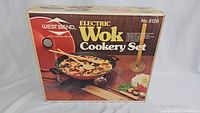 Front and side view of West Bend Electric Wok Cookery Set in original box showing product image, model number 5129, and branding.