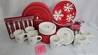 Full set of ceramic dishes and mugs, showing red plates with snowflakes, white mugs and smaller white plates with snowman designs, along with boxed sets of snowman spoons.