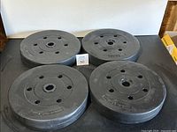 Four black 20 lbs weight plates displayed flat on a surface in a square formation.