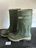 Side view of green rubber Cofra boots showing 'THERMIC', 'SUPER LIGHT', 'MADE IN ITALY' branding and rugged treaded yellow-soled base