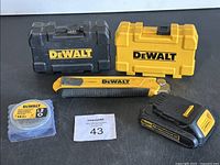 Overall lot showing two DeWalt cases, measuring tape, battery, and utility knife.