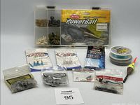 Full assortment of fishing tackle items displayed including tackle box, fishing hooks in packets, fishing line spool and float.