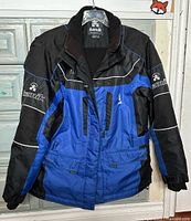 Full front view of the Kamik men's winter jacket in black and blue with white accents, showing pocket and zipper details.