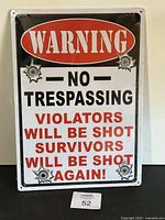 Front view of metal no trespassing warning sign with bold lettering and bullet hole graphics.