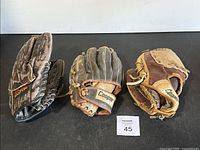 Three old baseball gloves arranged on black surface showing Cooper branding and wear details
