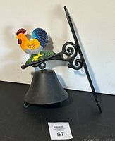 Photo of the entire roster dinner bell showing black metal bell, mounting bracket with rooster figurine on top.