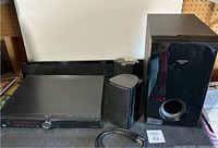 Photo showing the overall sound system setup including Blu-ray player, soundbar, subwoofer, two satellite speakers, and power cable.