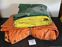 Folded green and yellow tarp showing peeling paint and wear on top of orange tarp