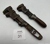 Two vintage adjustable wrenches laid flat, showing metal bodies with adjustable jaws and round wooden handles, displaying wear and patina.