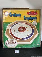 Photo of the original box showing the 'De Luxe Crokinole' branding and indications of 2 games in 1 including a checkerboard pattern.
