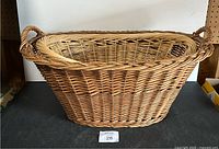 Side view of one wicker laundry basket showing the woven natural material, handles, and oval shape.