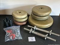 Weight plates stacked with dumbbell bars and black cone-shaped accessories on a black surface against a white wall.