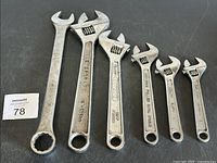 Six assorted metal wrenches including open-end/combo and adjustable wrenches placed on a black surface.