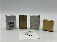 Full view of three Zippo lighters and a square brass-colored tape measure with Rolex branding