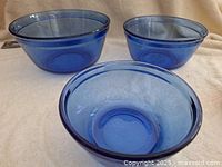 Three blue glass Anchor Hocking nesting mixing bowls arranged on white fabric