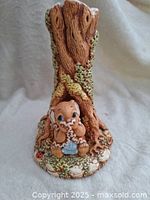 Front view of the ceramic Angie Little Rabbit figurine sitting under a tree trunk candle holder, showing detailed painted features and textured bark with moss.