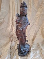 Front view of carved wooden Asian figurine, standing on a detailed base, holding an object in hand, showing overall condition and details.