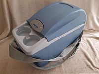 Closed blue and gray portable drink cooler showing top cup holders and carrying strap.