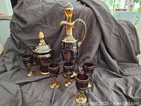 Full lot display showing tall red decanter with gold accents and five matching glasses on cloth background.