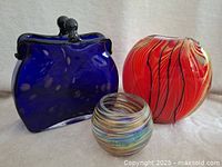 Photo of the three glass pieces together: blue purse-shaped piece, large red vase, small multicolor bowl.
