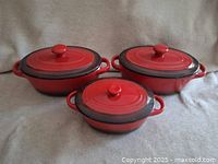 Three red Denby lidded baking dishes shown with lids on, placed on a neutral fabric background.