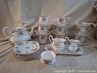 Full set of Royal Albert Petit Point china showing teapot, cups and saucers stacked, sandwich plates, cream and sugar set, and serving tray on neutral fabric background.