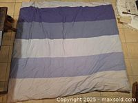 Top view photo of queen size goose down duvet with blue and light blue horizontal striped cover laid flat on tiled floor.
