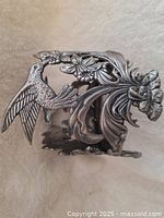Side view of pewter holder displaying a detailed bird with open wings and floral decoration.