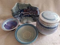 Set of 4 handcrafted pottery pieces including bowls, platter and lidded jar arranged together showing colors and shapes.