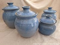 Four blue glazed pottery canisters with lids arranged in a group showing size variation and finish.