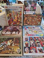 Lot photo showing array of seven 1000-piece puzzles with visible box art including dogs, floral scenes, bookshelf with cats, cowboy scene, and craft supplies.