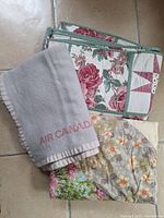Three textiles including two floral/geometric patchwork quilts and one gray Air Canada wool blanket with red logo.