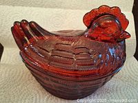 Front and side view of the red glass chicken dish with textured feather and comb details.