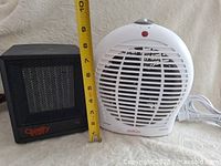 Two small space heaters side by side with measuring tape showing height of black heater.