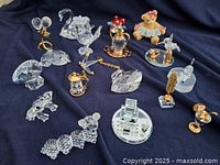 Overview of all 11 figurines arranged on dark cloth: mix of clear crystal and gold-tone accent pieces plus painted teddy bear