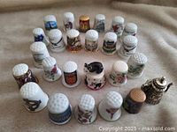 Set of 25 varied decorative thimbles displayed with designs showing animals, flowers, and coats of arms.