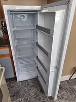 Open interior view showing four wire shelves, slide-out wire basket, temperature control dial and four grey-trimmed door bins on door