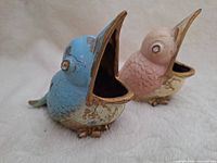 Front angle showing the two bird ornaments, blue and pink, with open beaks and jewel eyes.