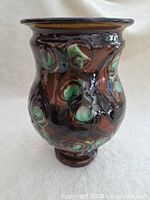 Photo showing front view of vintage pottery vase with dark brown glaze and green circular patterns.
