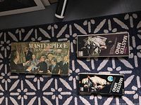 Top view of the three boxed games on carpet: large Masterpiece game box and two Master Mind game boxes, showing vintage themed artwork and knight chess piece graphics.