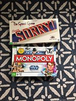 Classic Sorry and Star Wars Monopoly board game boxes stacked on patterned fabric.