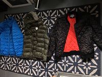 Three outerwear items laid out on carpet: bright blue Columbia jacket, olive green Gap vest with hood, black Lucky Brand jacket with red lining